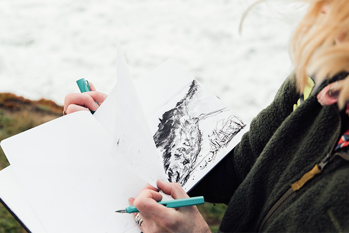 Emma Scattergood turning the pages of her sketchbook on the cliffs in Cornwall