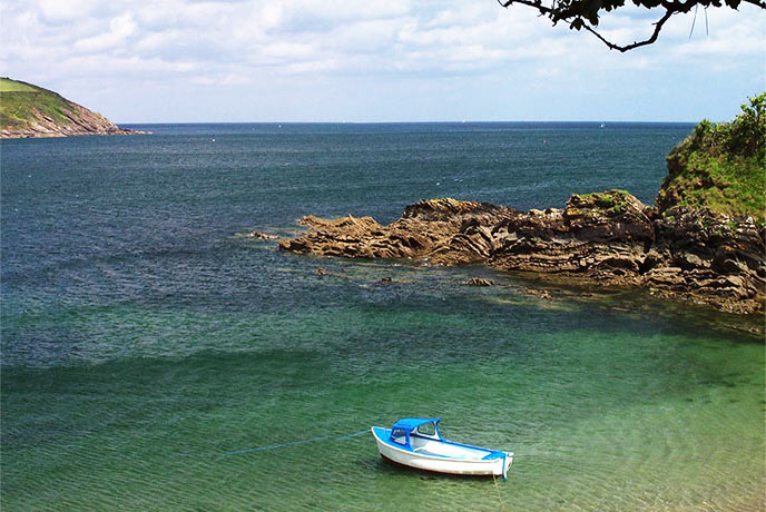 A boat bobbing in turquoise waters at Bosahan Cove on the Helford River
