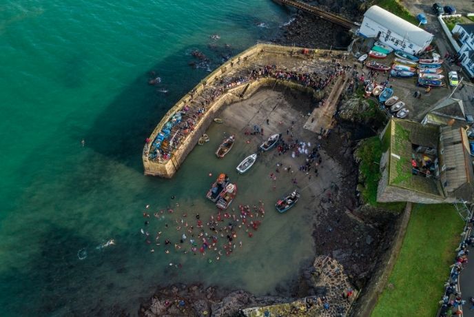 a bird's eye view of christmas day swimmers in the harbour at coverack