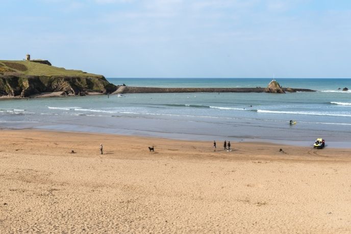 A wide shot of people and dogs walking on Crooklets Bay Beach in Cornwall