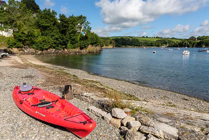 A red kayak on the pebble beach at Gillan Cove on the Helford River