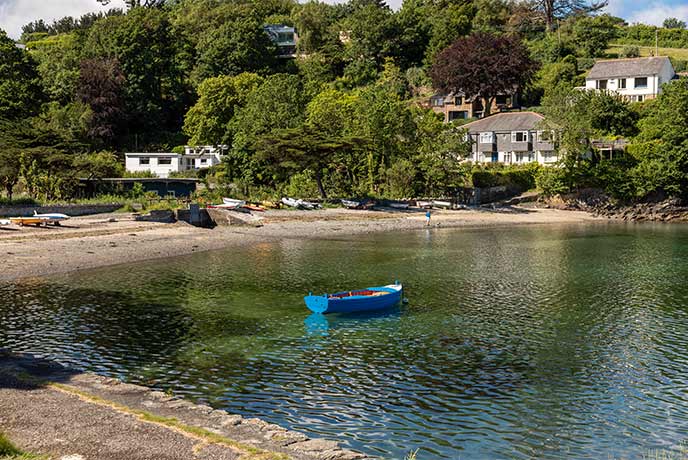 A pretty cove with cottages in the trees behind and boats in the water at Gillan Harbour Beach on the Helford River