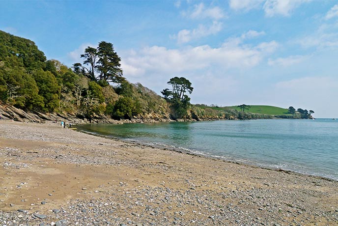 Looking across the sand and pebble beach at Grebe on the Helford River, with the water and trees in the background