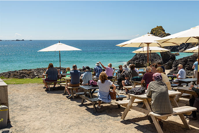 People sitting outside of Kynance Cove Cafe with the sea in the background