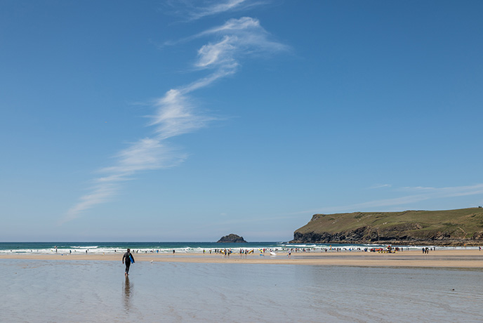 A person walking towards the sea across the sandy beach at Polzeath in Cornwall