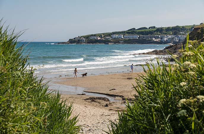 Peeking through greenery at the golden sands of Portscatho beach with the village in the background