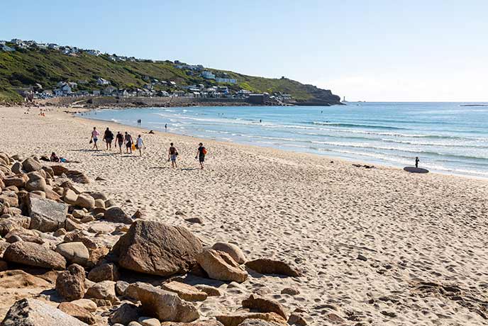 People walking along the golden sands of Sennen Beach on the South West Coast Path