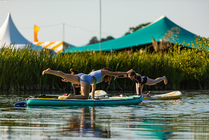 Two people doing yoga on SUP boards with tents behind them at Rock Oyster Festival
