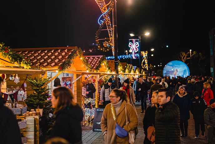 People walking past colourful stalls at night at the Truro Christmas Market in Cornwall