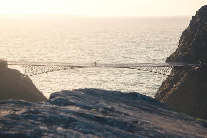 A couple crossing the bridge at Tintagel at sunset