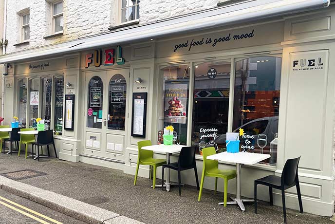 The light green exterior of Fuel café with brightly coloured tables and chairs outside on the pavement