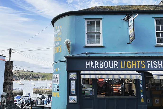 The bright blue exterior of Harbour Lights, with the harbour visible through the alley to the side