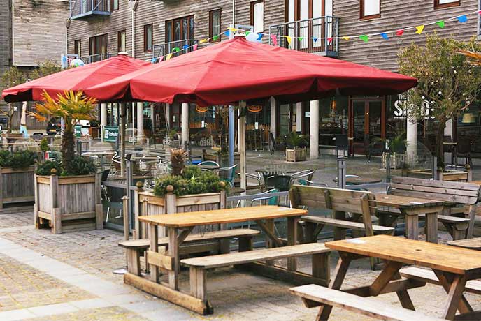 Wooden tables and parasols in the outside seating area at The Shed in Falmouth