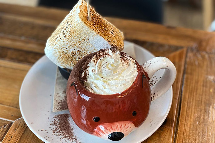 A cub hot chocolate topped with whipped cream with a giant marshmallow in a fox shaped mug at Slice of Cornwall