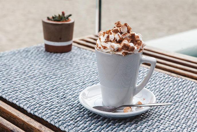 A hot chocolate with the beach in the background at Gylly Beach Café