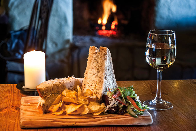 A plate of sandwiches and a glass of wine in front of an open fire at Pandora Inn