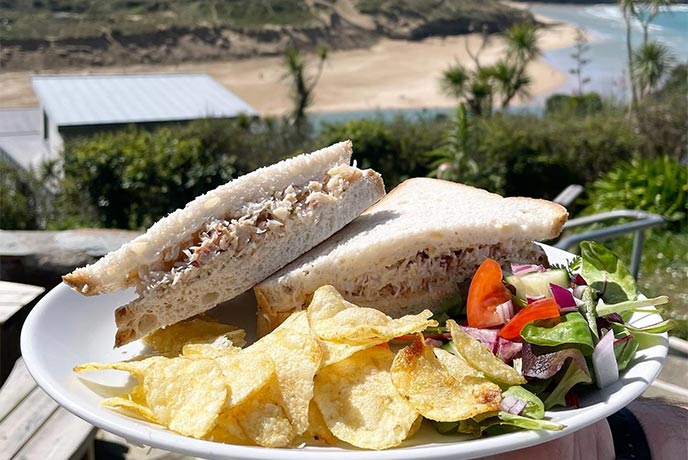 A plate with a crab sandwich, crisps, and salad overlooking the estuary at Fern Pit Café in Cornwall