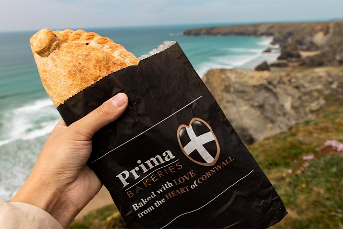 Some holding a Cornish pasty in a Prima Bakeries bag on the cliffs