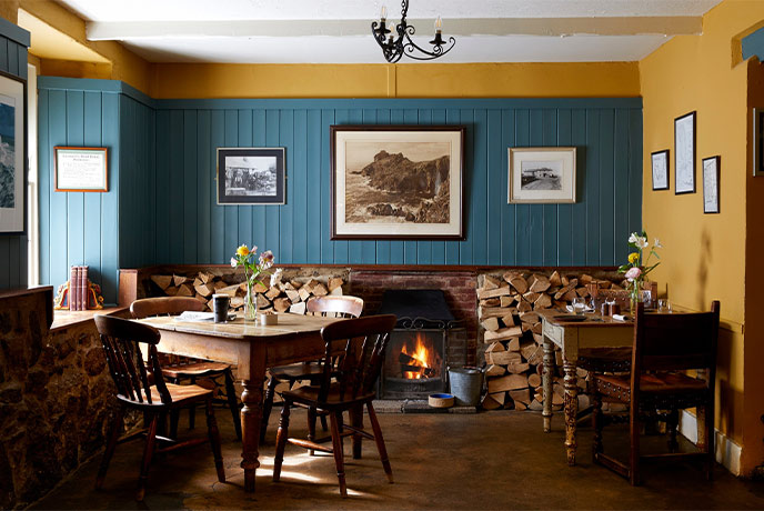 A cosy dining room at The Gurnard's Head with a fireplace, yellow walls and deep wood tables
