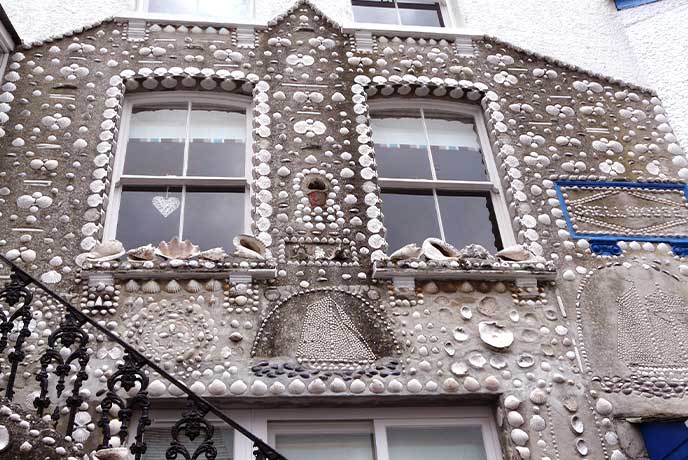 The unusual exterior of The Shell House in Cornwall, with hundreds of little shells stuck into the concrete in various patterns
