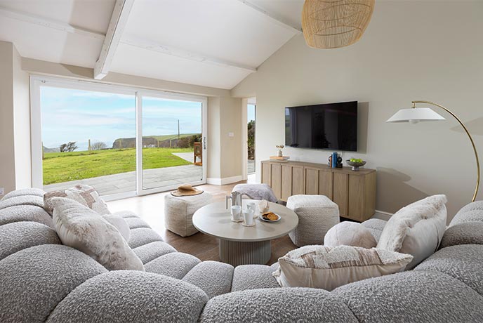 Curving grey sofas curl around a table overlooking countryside and ocean at Brockhill Chapel in Cornwall