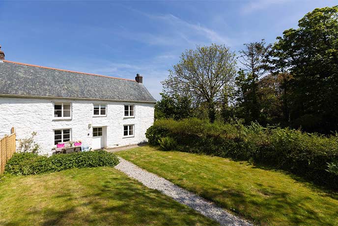 A pretty white-wash stone cottage with a grassy garden in Cornwall