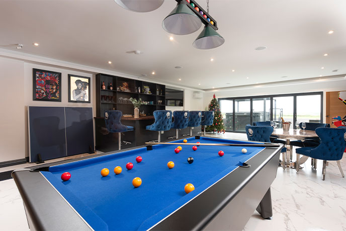 A billiards table in a modern styled games room in Cornwall with a sleek bar in the background