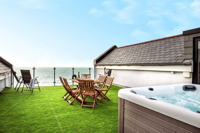 The terraced grass area with hot tub and seating overlooking the sea at Cormorant