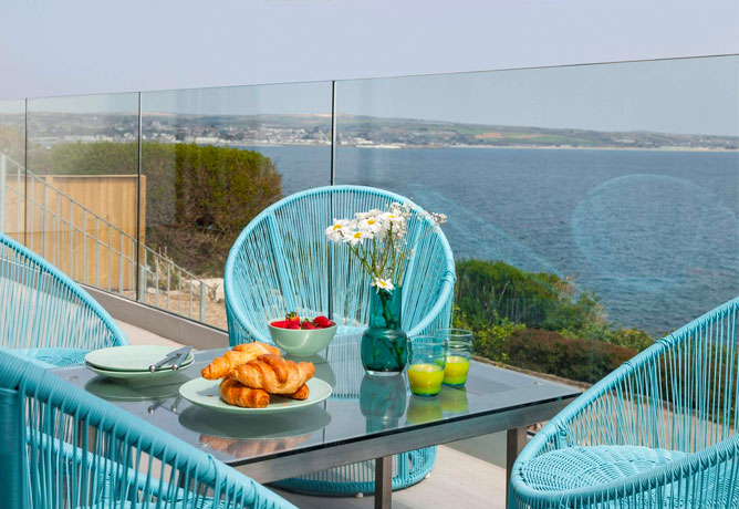 Bright blue chairs and a table on the terrace with the Cornish coast in the background