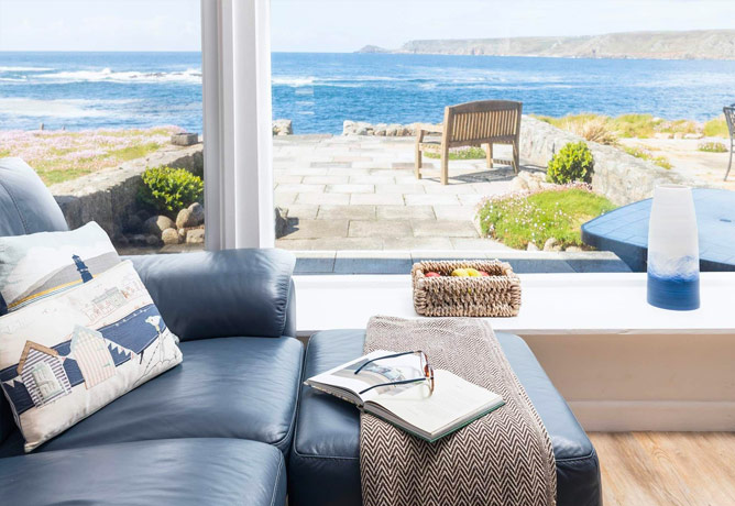 A deep blue sofa next to a window that looks out over the terrace and the sea behind