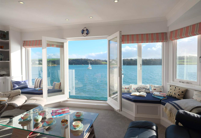 A spacious living room looks out over Falmouth harbour with a sailing boat in the distance