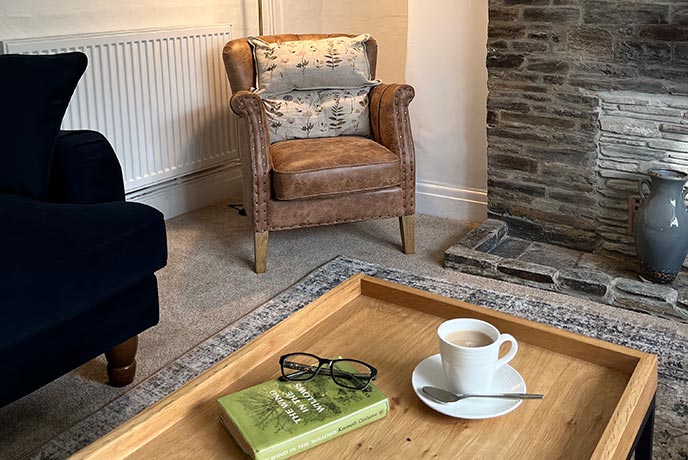 A coffee table with a cup of tea, book, and reading glasses on it at Tom's Cottage in Cornwall