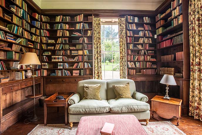 The cosy library at Tresillian House with floor to ceiling shelves stacked with books and a comfy armchair