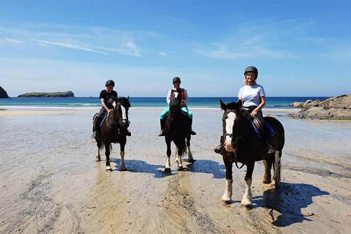 Three people on horses on the beach with Newton Equestrian