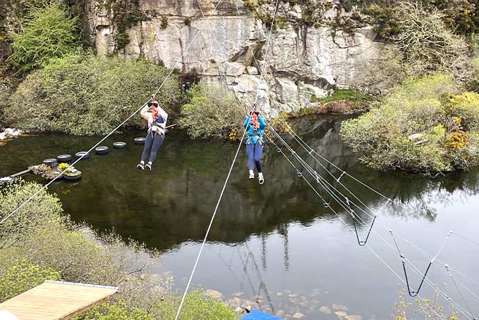 Two people flying over the water in the quarry on a zip wire at Via Ferrata