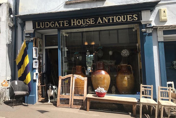 The exterior of Ludgate House Antiques with lots of antiques in the window and a dog standing in the door