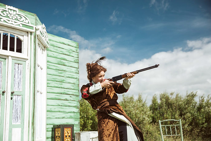 Actress Rose McPhilemy aiming a prop rifle during an outdoor performance of The Cherry Orchard by Miracle Theatre