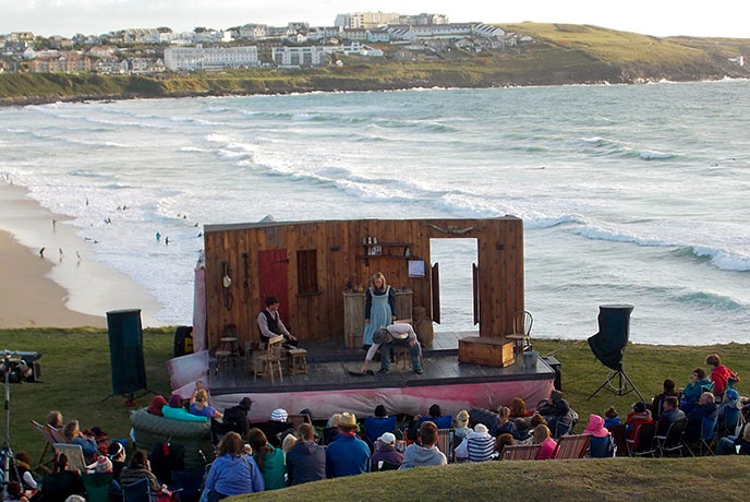 An outdoor performance of The Magnificent Three by Miracle Theatre at the Headland Hotel with Fistral beach in the background