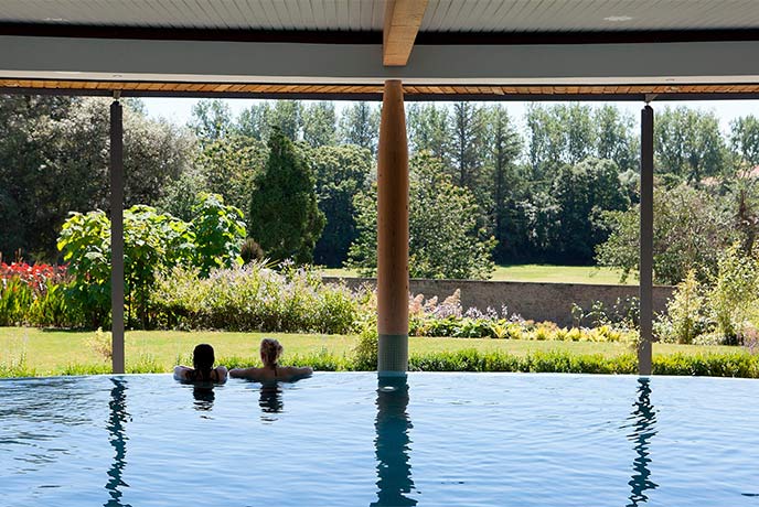 People at the edge of the swimming pool looking out over the gardens at The Cornwall Spa