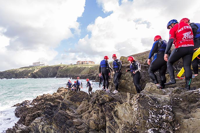 A group of people coasteering around the cliffs at Newquay in North Cornwall