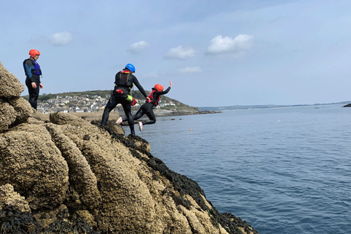One of the team jumping off the rocks around Mousehole into the sea with the Global Boarders team there to help