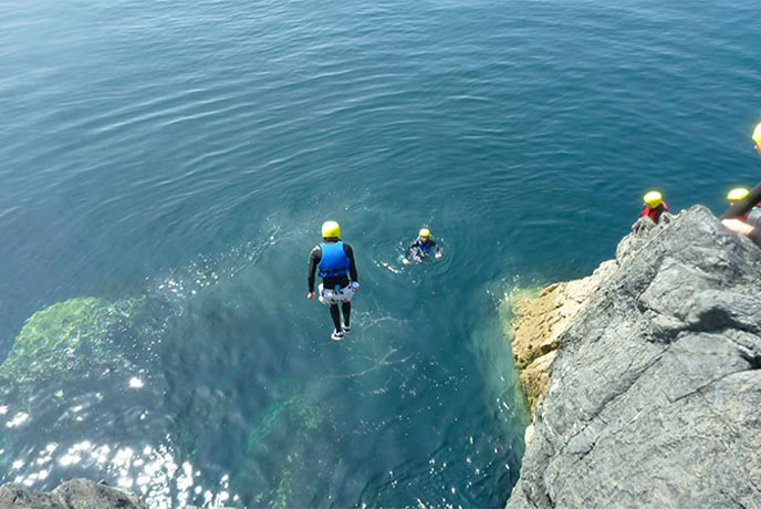 People jumping into the sea from cliffs while wearing hard hats and wetsuits