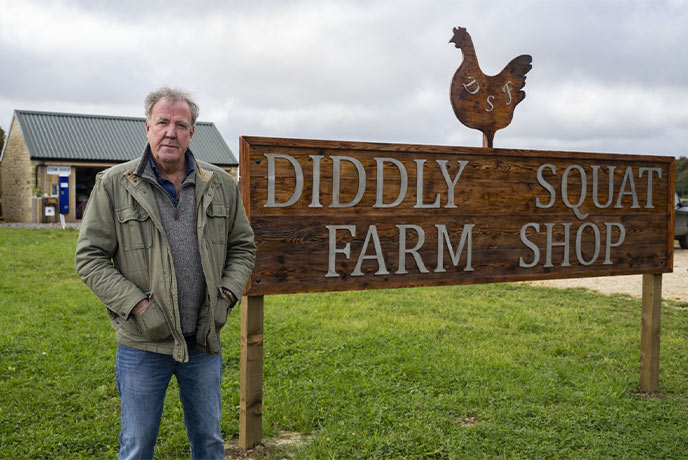 Jeremy Clarkson standing next to the Diddly Squat Farm Shop sign in the Cotswolds