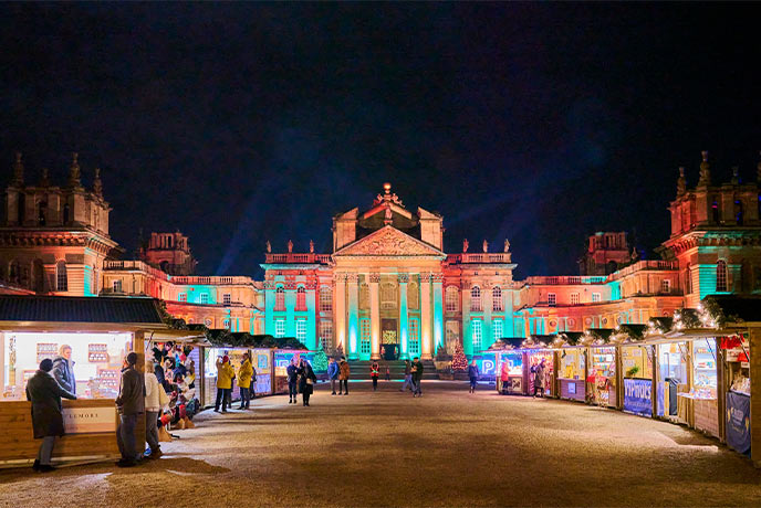 Blenheim Palace lit up with colourful lights and stalls in the court below at the Christmas Market