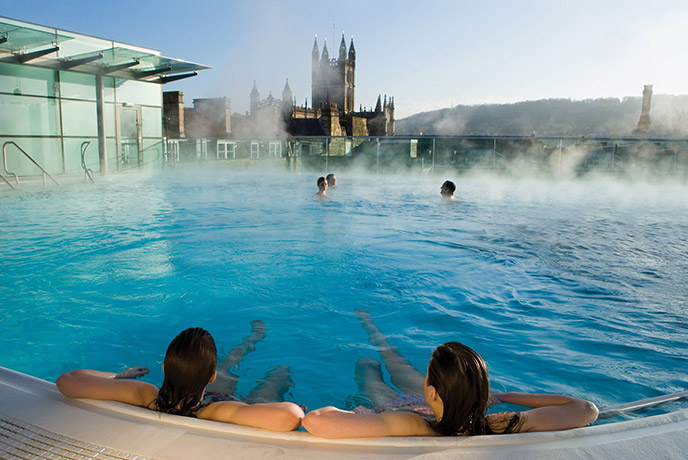 People relaxing in the rooftop pool with the skyline of Bath in the background at Thermae Bath Spa
