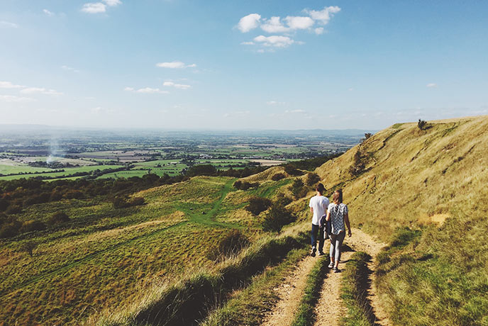 Two people walking along The Cotswolds Way with the rolling countryside sprawling out in front of them