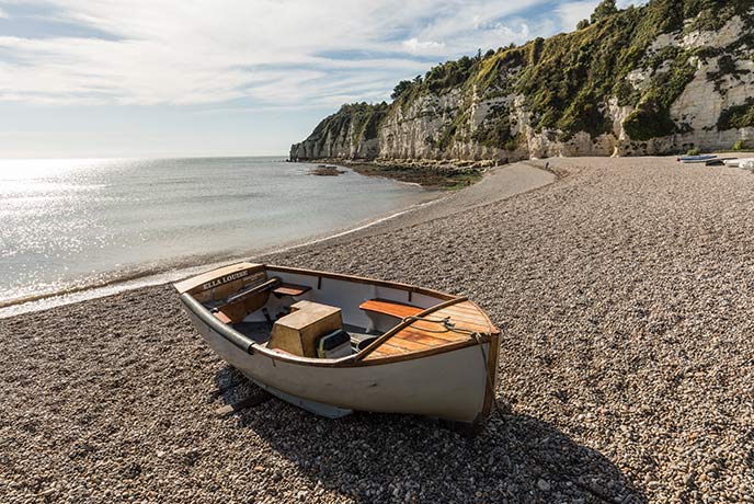 A boat moored on the beach at Beer, with white cliffs in the distance