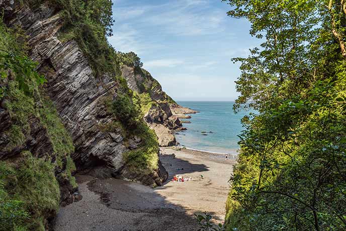 Looking through the trees at the beautiful shingle beach at Broad Sands on the South West Coast Path