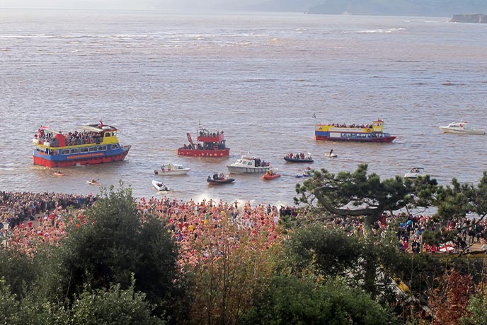 The beach at Exmouth covered in Christmas Day swimmers while the cruise bobs past
