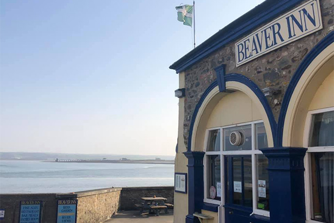 The stone exterior of The Beaver Inn with the sea behind